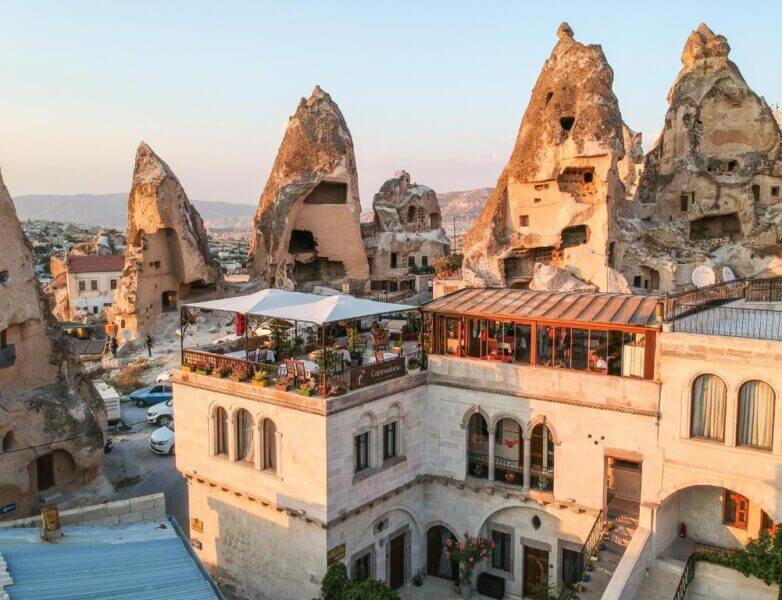 Rooftop restaurant on a stone building with unique rock formations and cave dwellings in the background, likely in Cappadocia, Turkey—perfect for enjoying sunset views over this stunning cave hotel landscape.