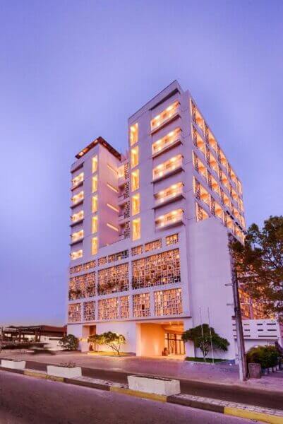 A modern multi-story hotel building, Jetwing Jaffna, features illuminated balconies and a geometric facade, pictured at dusk beneath a clear sky.