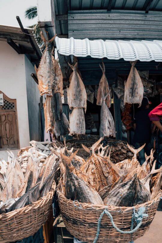 Baskets and racks of dried fish on display at an outdoor market stall in Trincomalee, Sri Lanka.