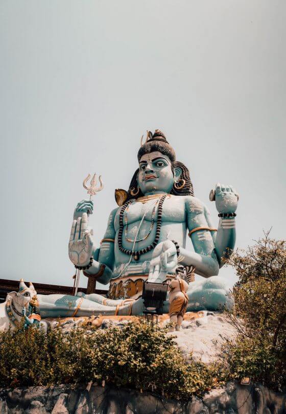 Large statue of Lord Shiva in a seated pose, holding a trident and drum with a cobra around his neck, set outdoors against a clear sky at the renowned Koneswaram Temple in Trincomalee.