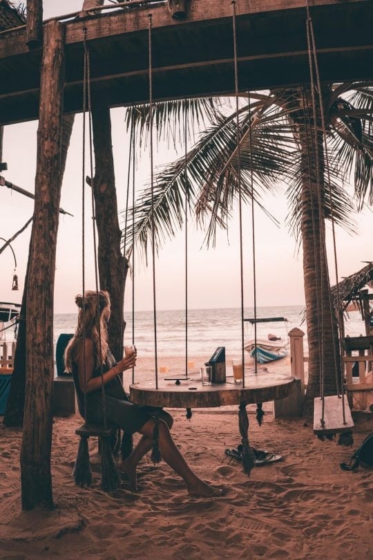 A person sits on a wooden swing under a beachside structure at Fernando