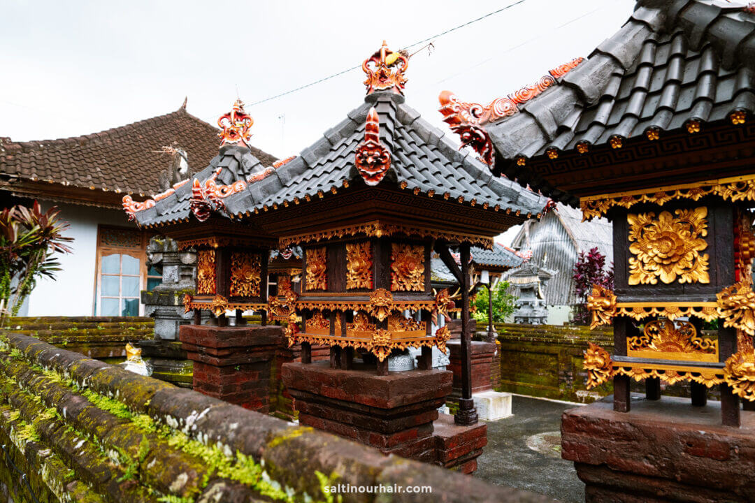 Ornate Balinese Hindu shrines with intricate gold and red decorations stand in a courtyard surrounded by stone walls and tiled roofs, offering a glimpse of traditional culture often found at a serene homestay Bali experience.