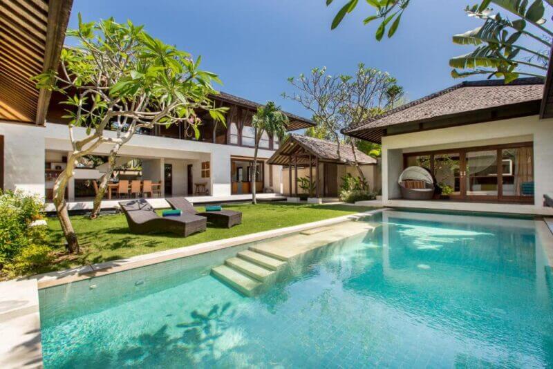 Modern Seminyak villa with a private pool, lounge chairs, open dining area, and landscaped garden under a clear blue sky.