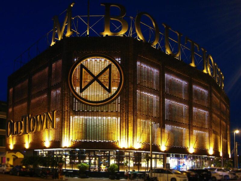 A modern building with M BOUTIQUE and OLD TOWN signage, illuminated by yellow lights at night, features a large circular logo on the facade and reflects the stylish charm of m-boutique ipoh.