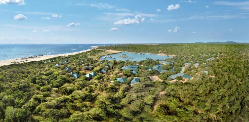 Aerial view of Cinnamon Wild Yala, a coastal resort surrounded by lush vegetation, a lagoon, and the ocean to the left under a blue sky—perfect for your Sri Lanka safari adventure.
