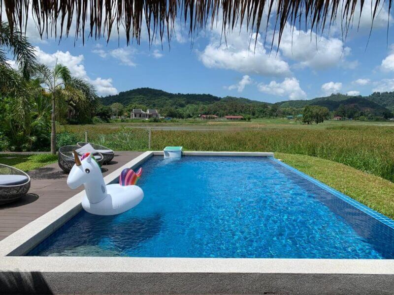 A rectangular pool with a unicorn float is set beside a grassy field at a Langkawi hotel, overlooking distant hills under a partly cloudy sky—a true cloud9 escape.