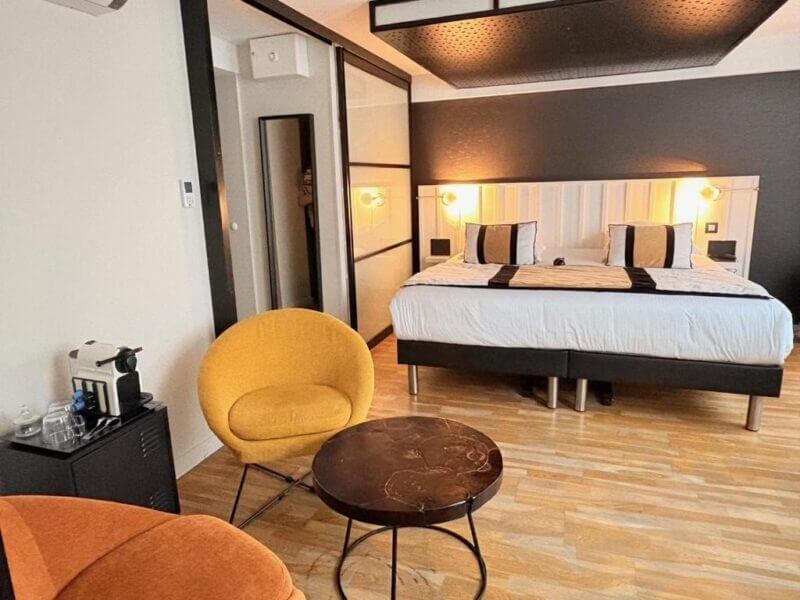 Modern hotel room in La Rochelle with a double bed, two round yellow chairs, a small dark fabrique table, wood flooring, and a coffee machine on a side table.