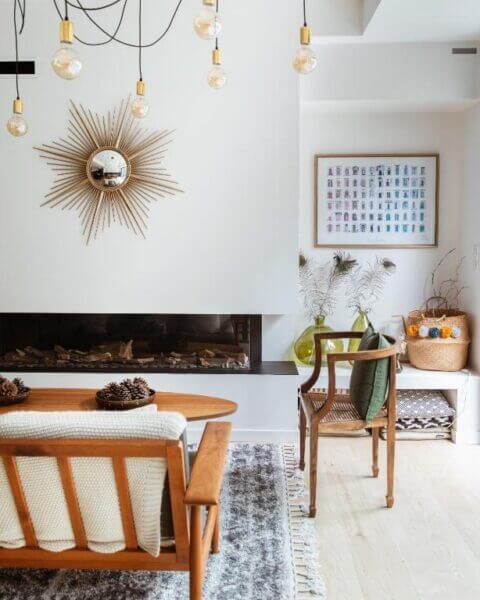 A mid-century modern living room at La Maison Odeia in Bordeaux features wooden furniture, a wall-mounted sunburst mirror, a fireplace, pendant lights, and decorative baskets and artwork.