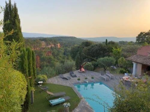 A backyard with a swimming pool, lounge chairs, and decking reminiscent of terrasse des ocres overlooks a green valley with hills in the distance under a hazy sky, evoking the charm of Roussillon.
