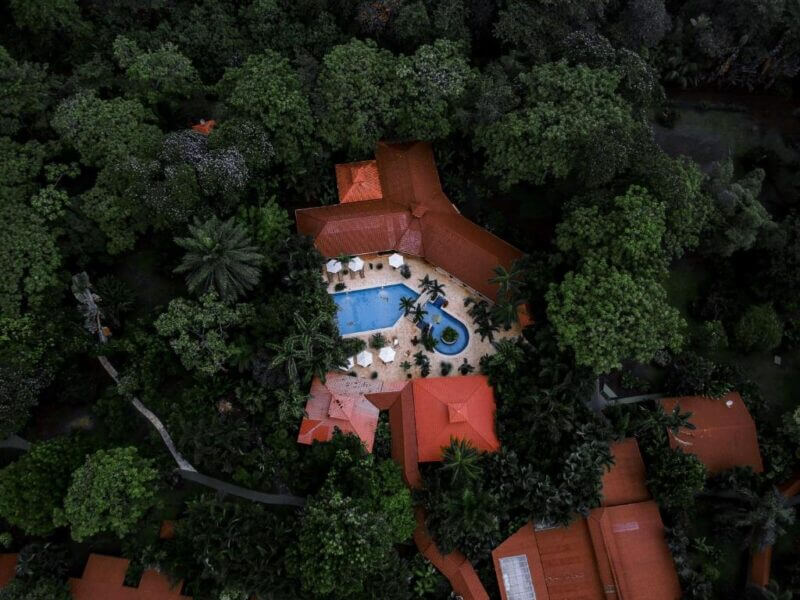 Aerial view of an eco lodge villa with terracotta roofs surrounded by dense greenery in Tortuguero, featuring a central swimming pool with lounge chairs and umbrellas.