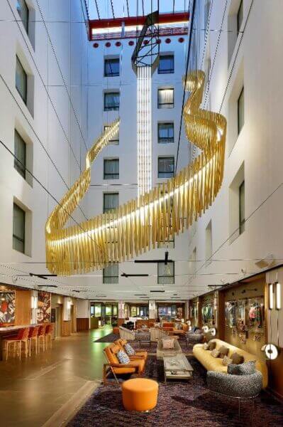 A modern hotel lobby at Hard Rock Madrid features eclectic furniture, a patterned rug, and a large, sculptural gold light fixture suspended from the ceiling.