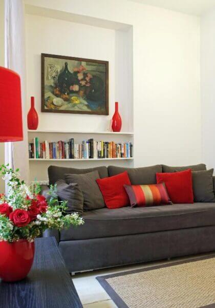 A modern Bac St. Germain apartment living room with a gray sofa, red accent pillows, a bookshelf, a painting, and stylish red decorative items including a lamp and flower vase.