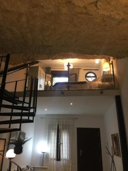 A view of a two-level Casa Cueva apartment with a spiral staircase, a lower living area, and an upper loft bedroom beneath a textured stone ceiling—embracing the unique charm of living in a cueva.
