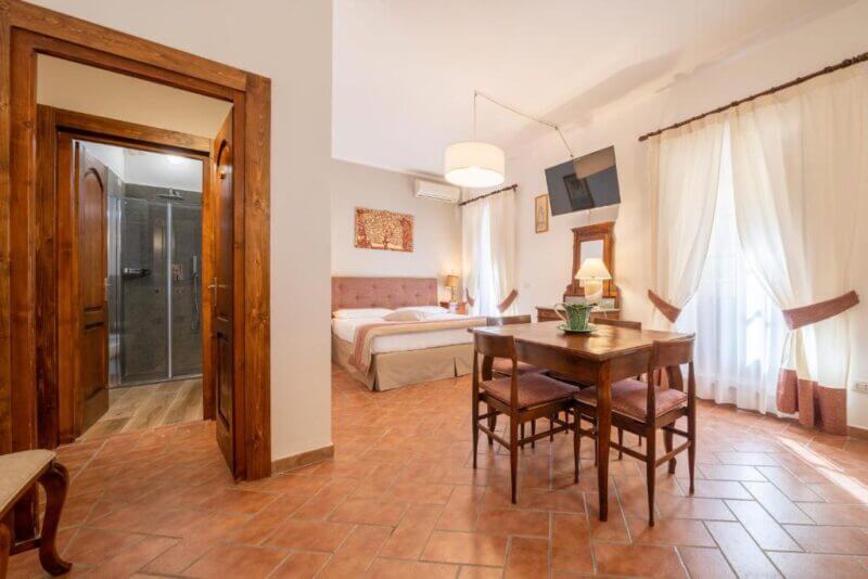 Bright accommodation at Affittacamere Valentina featuring a double bed, dining table and chairs, wall-mounted TV, large window with curtains, and an open doorway to a modern bathroom.