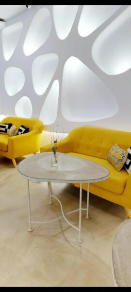 A modern lounge in Suite Generis with yellow sofas, geometric pillows, a round white table, and a decorative wall featuring abstract, illuminated shapes—perfect for any Hotel Boutique experience.
