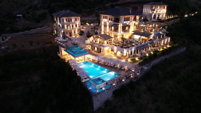 Kerculla Resort in Gjirokaster is a large, multi-level hotel complex illuminated at night, featuring outdoor pools, terraces with seating, and landscaped grounds surrounded by hills.