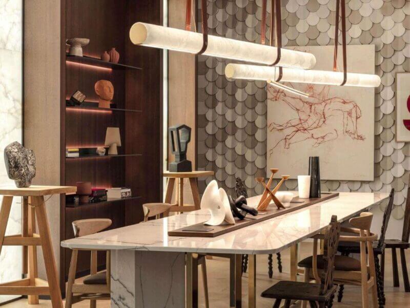 Modern dining room at L'Esquisse Hotel in Colmar, featuring a marble table, sculptural decor, wooden chairs, and contemporary lighting. Artwork and sculptures adorn the walls and shelves for a refined ambiance.