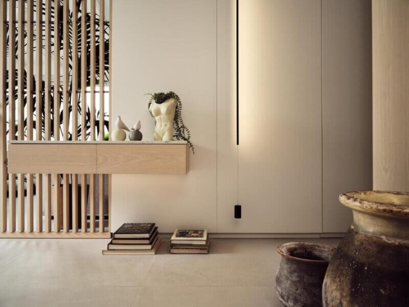 Modern minimalist interior inspired by Athens, featuring a floating wooden shelf, decorative bust, stacked books, potted plants, and two large rustic pots. Vertical slats divide the space in this Pallineon House setting.