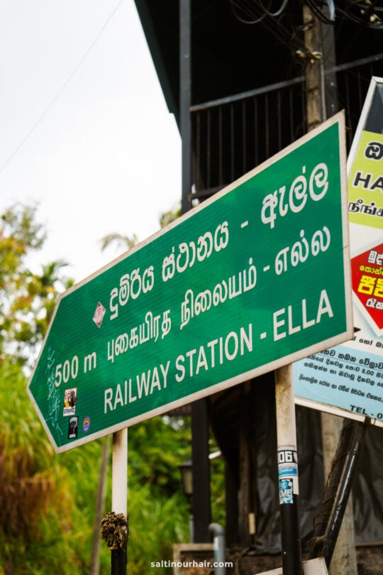 A green signboard indicating Railway Station - Ella Sri Lanka in multiple languages, with an arrow pointing left and 500 m distance noted.
