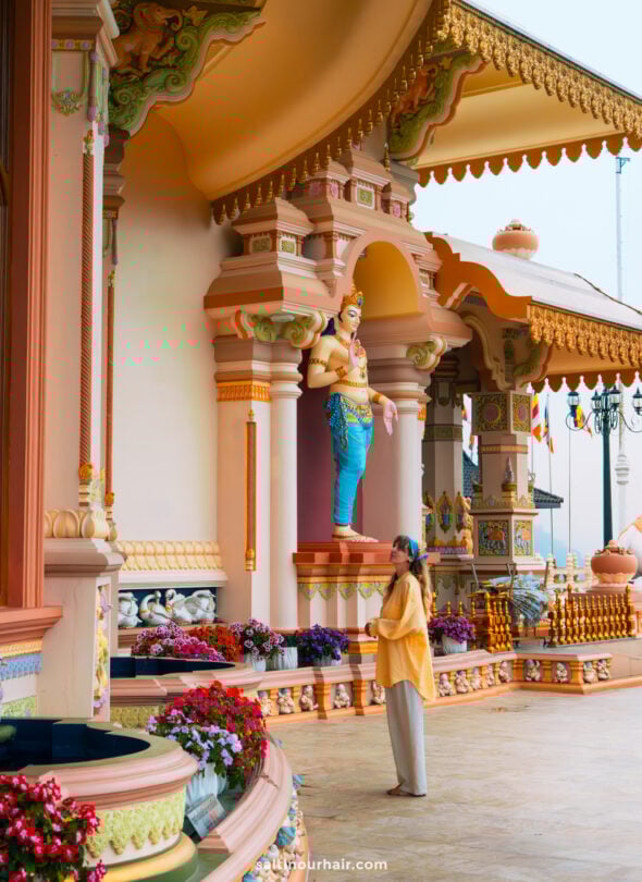A person stands in front of a colorful, ornate temple adorned with statues, columns, and flowers in Ella, Sri Lanka.