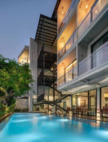 Modern POR hotel with balconies overlooks a ground-floor outdoor swimming pool, warmly lit at dusk, just minutes from Chiang Mai’s iconic Thapae Gate.