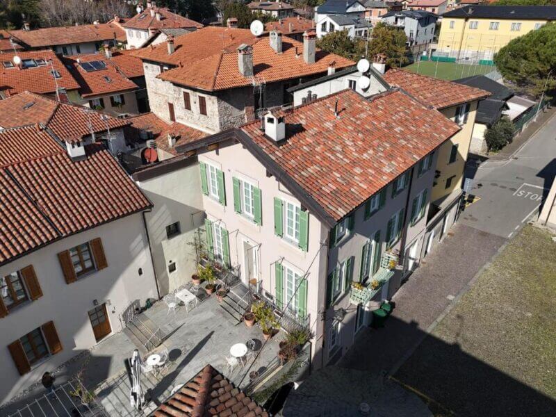 Aerial view of a residential area near Lake Como, featuring red-tiled roofs, a courtyard with tables and chairs, and several buildings along a narrow street, including the charming Locanda Alberti.