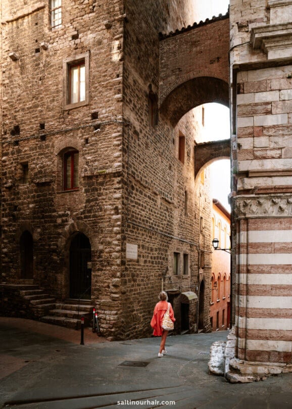 A woman in a red dress walks down a narrow, cobblestone street lined with old stone buildings—capturing the charm and allure of historic European towns, much like those you