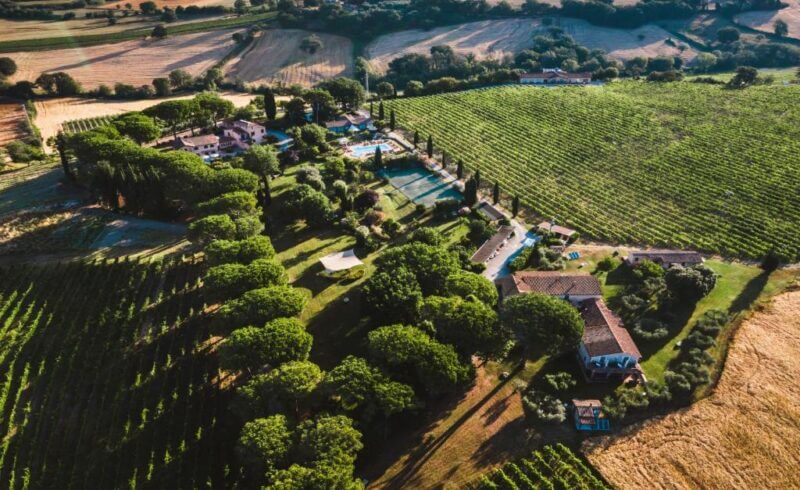 Aerial view of Villa Acquaviva near Montemerano, featuring a countryside estate with multiple buildings, a swimming pool, and surrounding fields, trees, and vineyards.