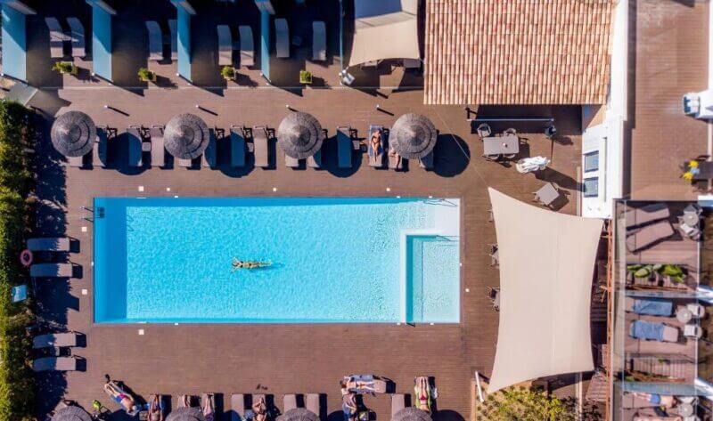 Aerial view of a rectangular outdoor swimming pool at the Atlantic Hotel in Lagos, Algarve, with lounge chairs and sun umbrellas around it; one person is floating in the pool.