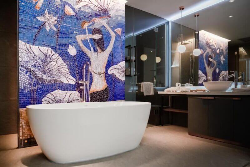 Modern bathroom in a Ho Chi Minh HOME, featuring a white freestanding tub, large mirror, and vibrant mosaic wall art depicting a woman surrounded by water lilies.