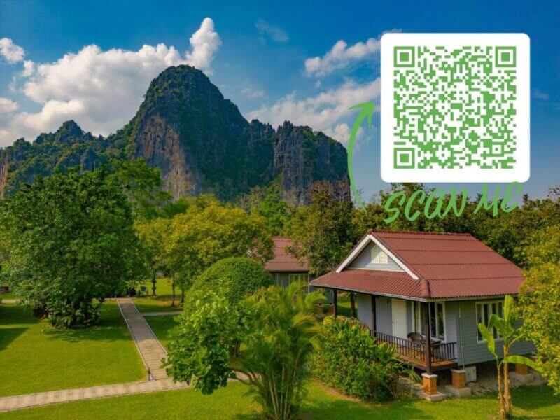 Cottage with a porch surrounded by trees and mountains under a blue sky, reminiscent of Bearlin Bungalow in Vang Vieng; a large green QR code with “scan me” is overlaid in the top right corner.
