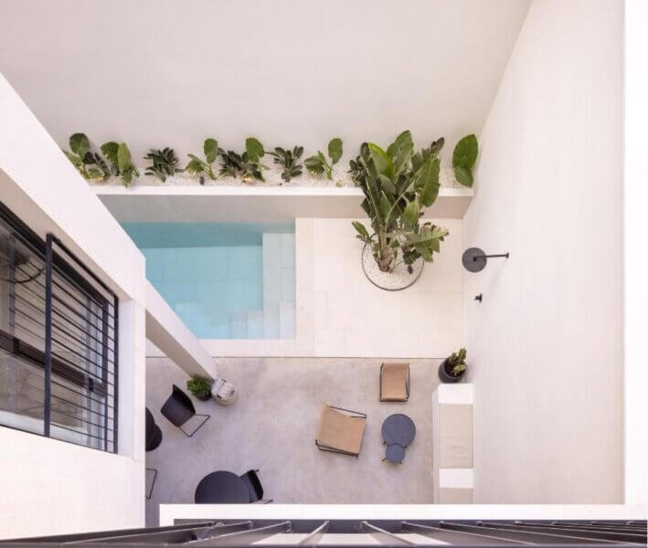 A modern courtyard at YOURS Valencia seen from above, featuring a small pool, potted plants, a seating area with chairs and tables, and a row of green plants along the wall.