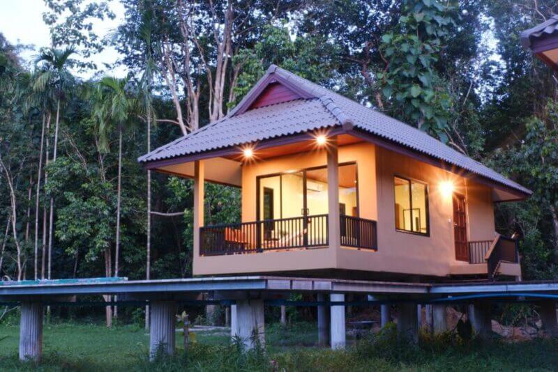 Charming boutique lodge with a tiled roof and lit porch, nestled among dense green trees in the forested Khao Sok area.