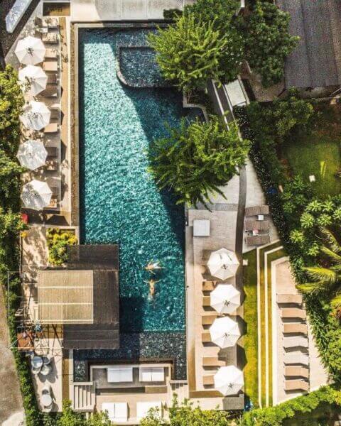 Aerial view of the rectangular swimming pool at Anana Eco Resort in Krabi, surrounded by lounge chairs, umbrellas, lush greenery, and two people swimming.