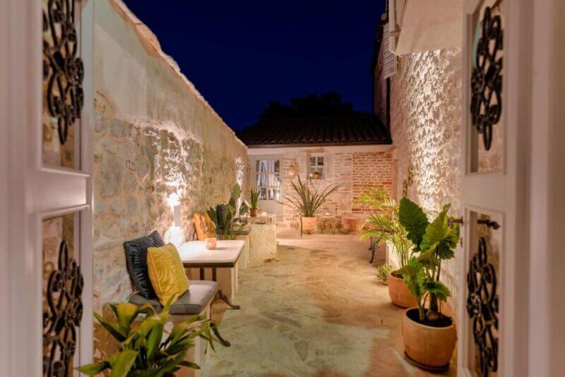A stone courtyard at night in Stari Grad, featuring potted plants, a cushioned bench, and soft lighting illuminating the textured walls of the charming town house.