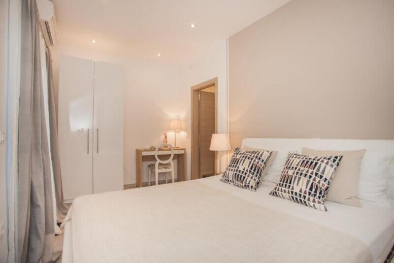 Minimalist bedroom with a double bed, geometric pillows, a wardrobe, a desk with a chair, and neutral decor—ideal accommodation in Sibenik at Hostel Splendido Sibenik.