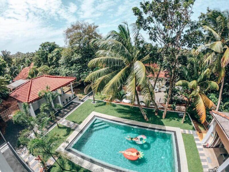 Aerial view of a backyard swimming pool at Green Hill Mirissa, with two people on inflatable pool floats, surrounded by palm trees and a tiled patio area—the perfect Sri Lanka accommodation for relaxation.