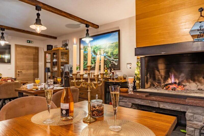 A cozy dining room at Villa Sumrak B&B in Plitvice, featuring a lit fireplace, set table with wine, candles, champagne glasses, and warm ambient lighting.