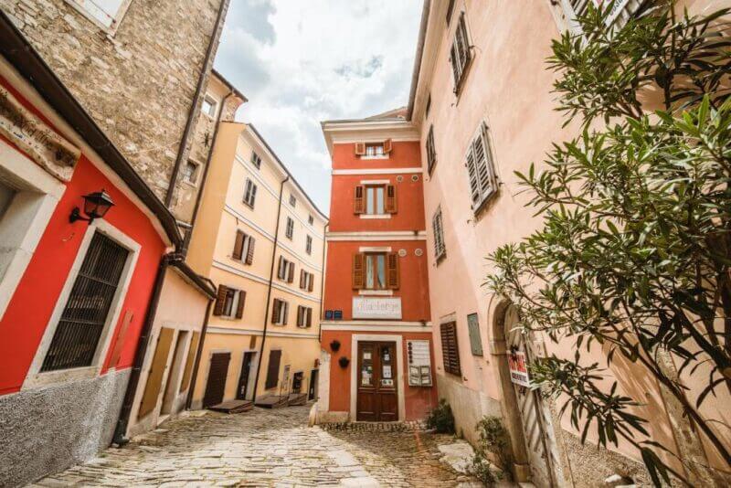 Narrow stone-paved street in Motovun, lined with colorful, old buildings; windows with shutters and a small tree on the right side, just steps from Villa Borgo BnB.