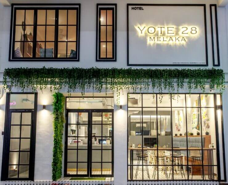 Exterior view of Yote 28 Melaka hotel with large windows, greenery above the entrance, and a visible seating area inside welcomes guests to the stylish Yote 28 Melaka experience.