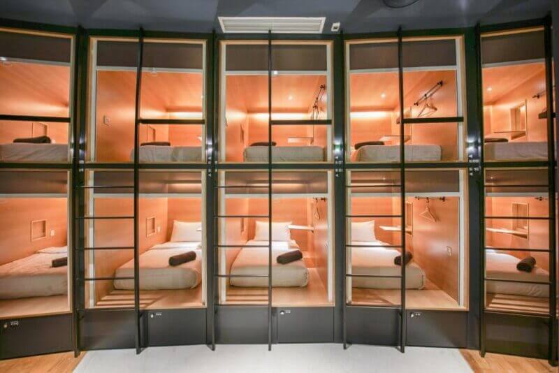 A row of modern capsule hotel sleeping pods, each with a bed, bedding, and lighting, offers smart budget accommodation in two vertical levels with ladders for access—perfect for travelers seeking a stylish Kuala Lumpur hostel near Bed KLCC.