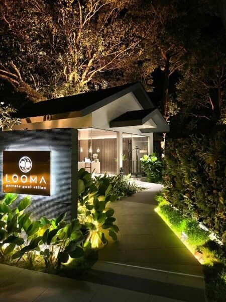 Night view of a modern Looma Villas entrance in Langkawi, surrounded by lush greenery, with a lit sign that reads Looma private pool villas.