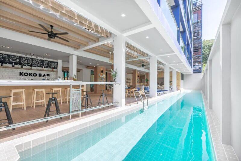 A modern outdoor bar and lounge area at Oasis Krabi, next to a narrow rectangular swimming pool with turquoise water, under a covered terrace.