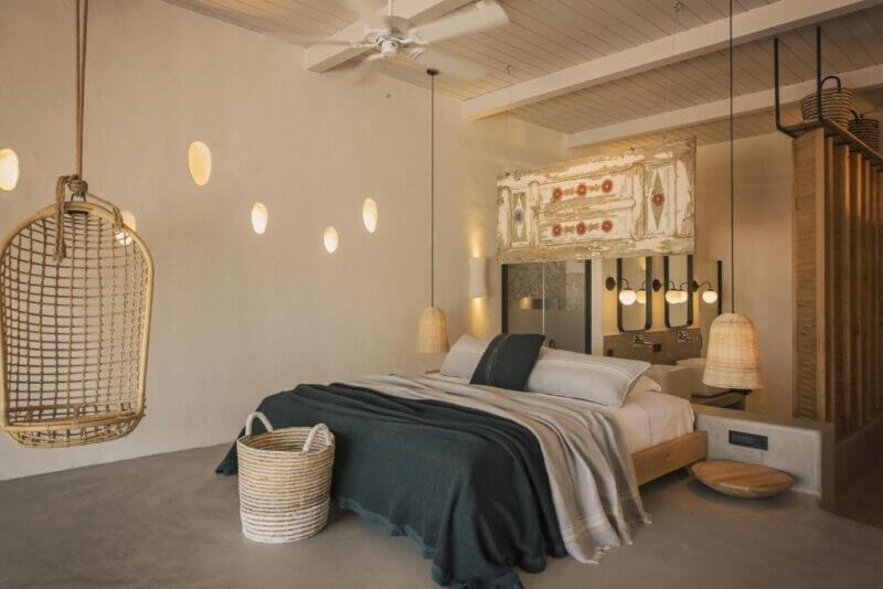 Minimalist bedroom at Yacht Boheme Hotel with a floating bed, hanging wicker chair, woven basket, and soft lighting; neutral tones and modern decor elements create a serene Fethiye retreat.