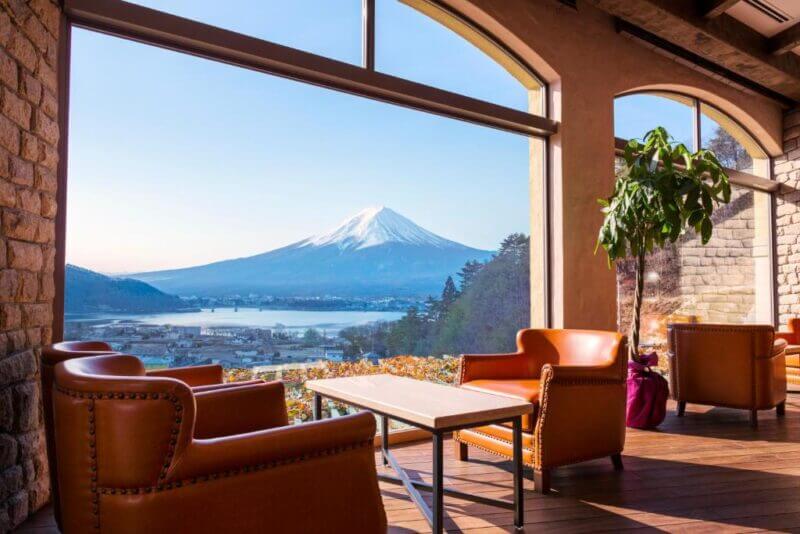 Lounge area with brown leather chairs and a large window offering a clear view of Mount Fuji, a lake, and a distant bridge—an inviting retreat at La Vista Fuji, your ideal Mount Fuji hotel for memorable stays.