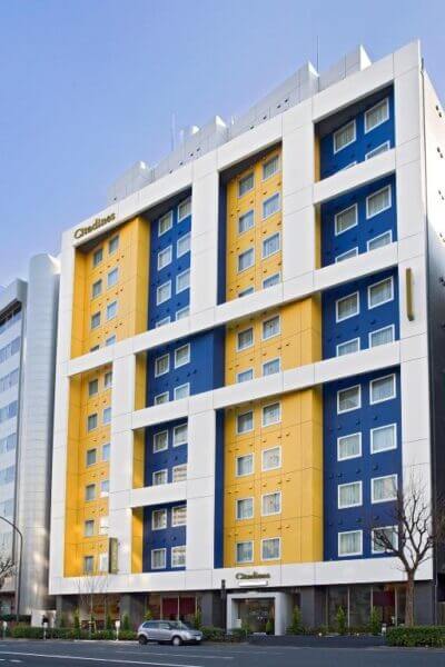 A modern mid-rise hotel building with a blue, white, and yellow facade, featuring many rectangular windows and the name Citadines displayed at the entrance in vibrant Shinjuku, Tokyo.