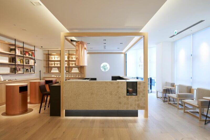 Modern cafe interior with minimalist design, light wood floors, neutral tones, a central counter, seating areas, and shelves displaying items along the walls—perfect for guests seeking stylish Tokyo accommodation at HOTEL 1899 TOKYO.