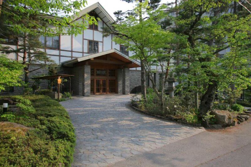 Stone pathway leading to the entrance of Senjukaku, a traditional-style ryokan in Shibu Onsen, surrounded by greenery and trees.