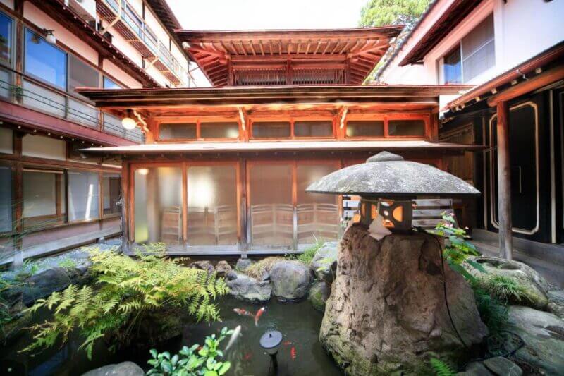 A traditional Japanese courtyard at Seifuso ryokan in Yudanaka, with a stone lantern, koi pond, and wooden building featuring shoji screens and overhanging roofs.