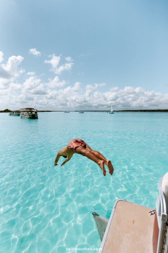 men diving from boat in tropical blue water bacalar lagoon mexico